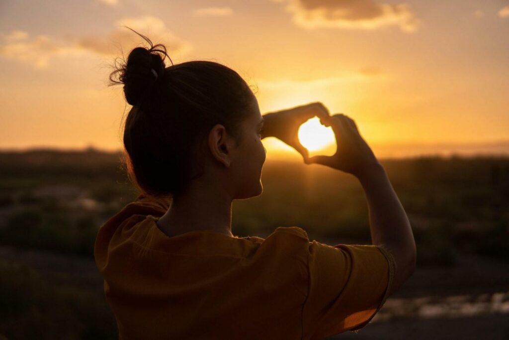Frau im Sonnenuntergang mit Herzhänden